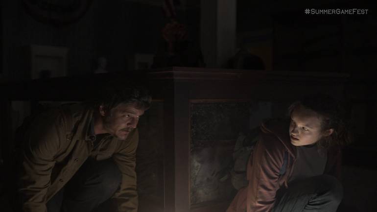 Cena da série de The Last of Us mostra Joel e Ellie se escondendo de um clicker atrás de uma mesa 