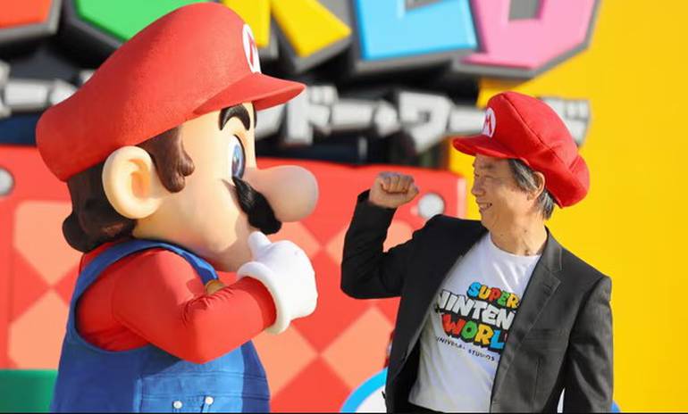 Foto mostra Shigeru Miyamoto comprimentando o Mario no parque tematico Super Nintendo World