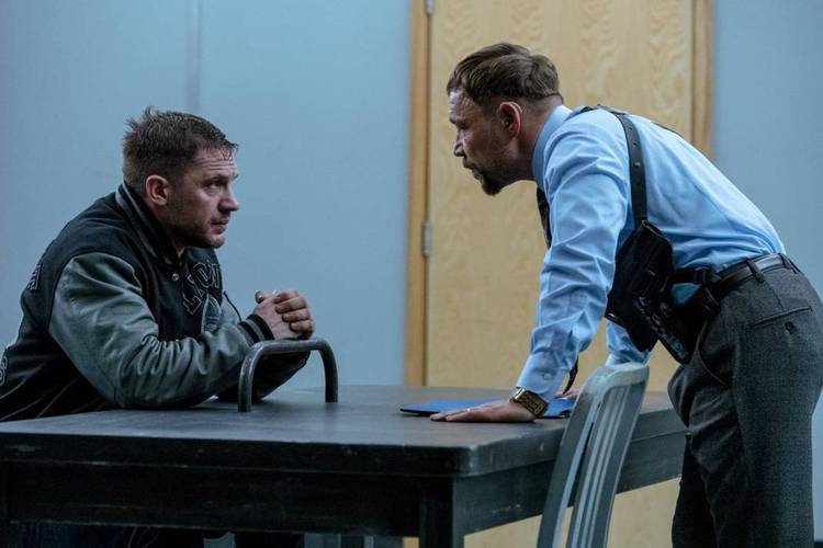 Tom Hardy sentado em uma mesa, sendo interrogado por Stephen Graham