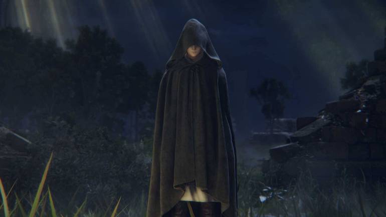 Cena do trailer de Elden Ring mostra Melina, uma mulher branca misteriosa que usa uma capa preta que cobre metade de seu rosto. Ela se encontra em um campo das Terras Intermédias a noite.