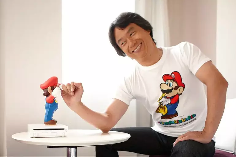 Foto de Shigeru Miyamoto comprimentando um boneco do Mario 